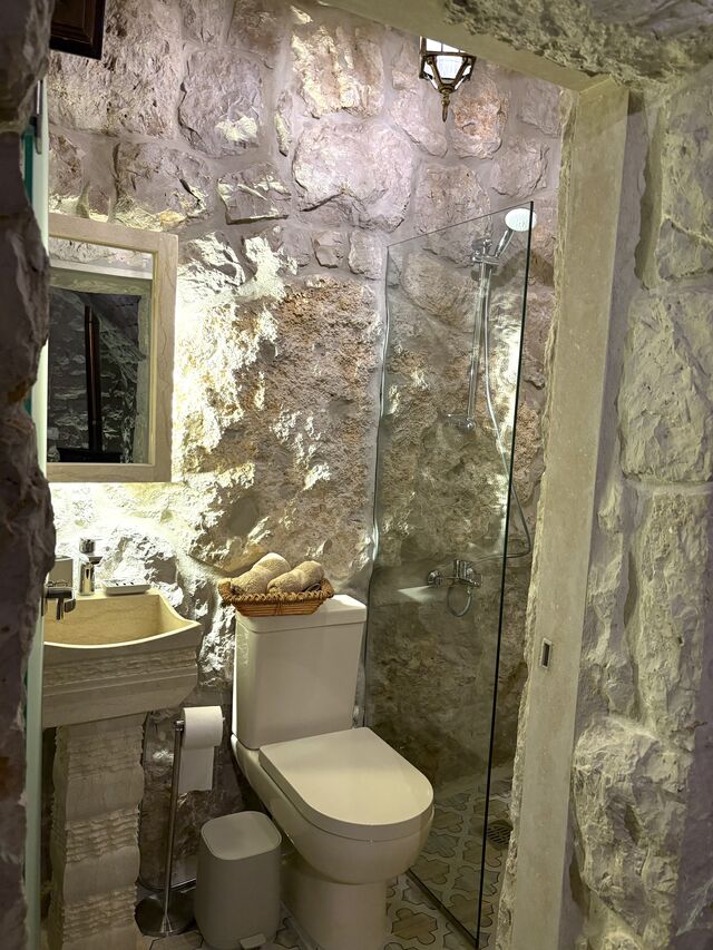 Gemelli's ensuite bathroom, glass shower panel against the stone wall beside the sink and toilet.