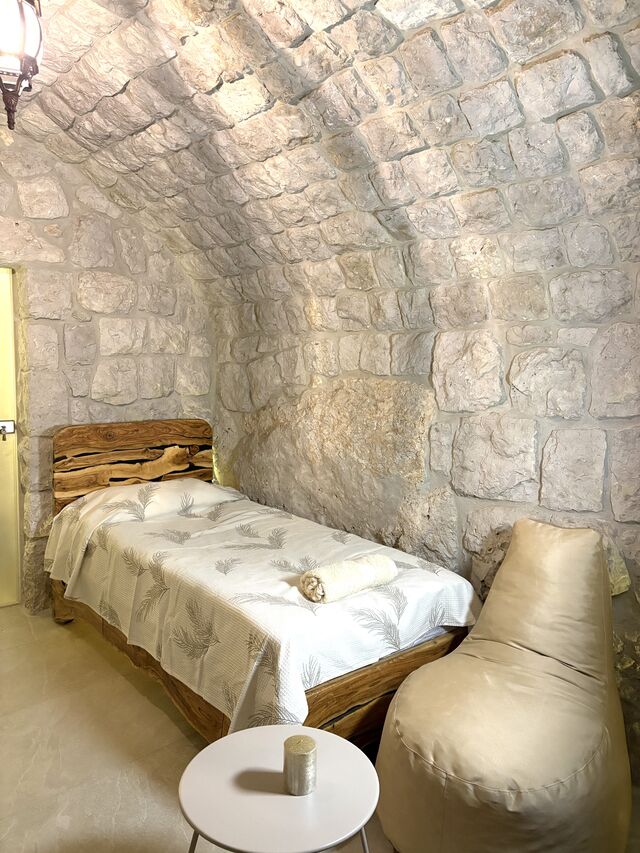 One of the two single beds in Gemelli, raw timber frame against the stone wall.