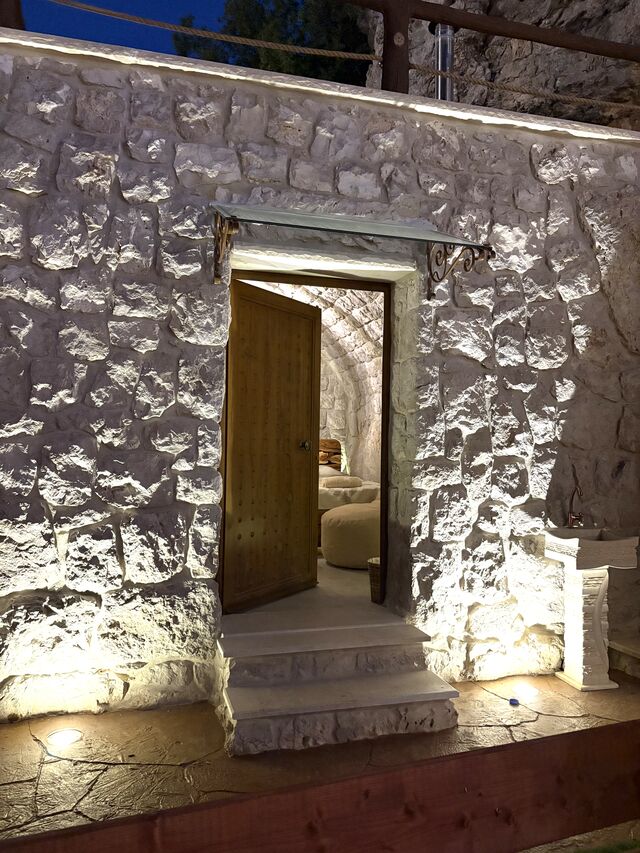 Gemelli's entrance at night, a timber door set into the stone facade at the lower end of the property.