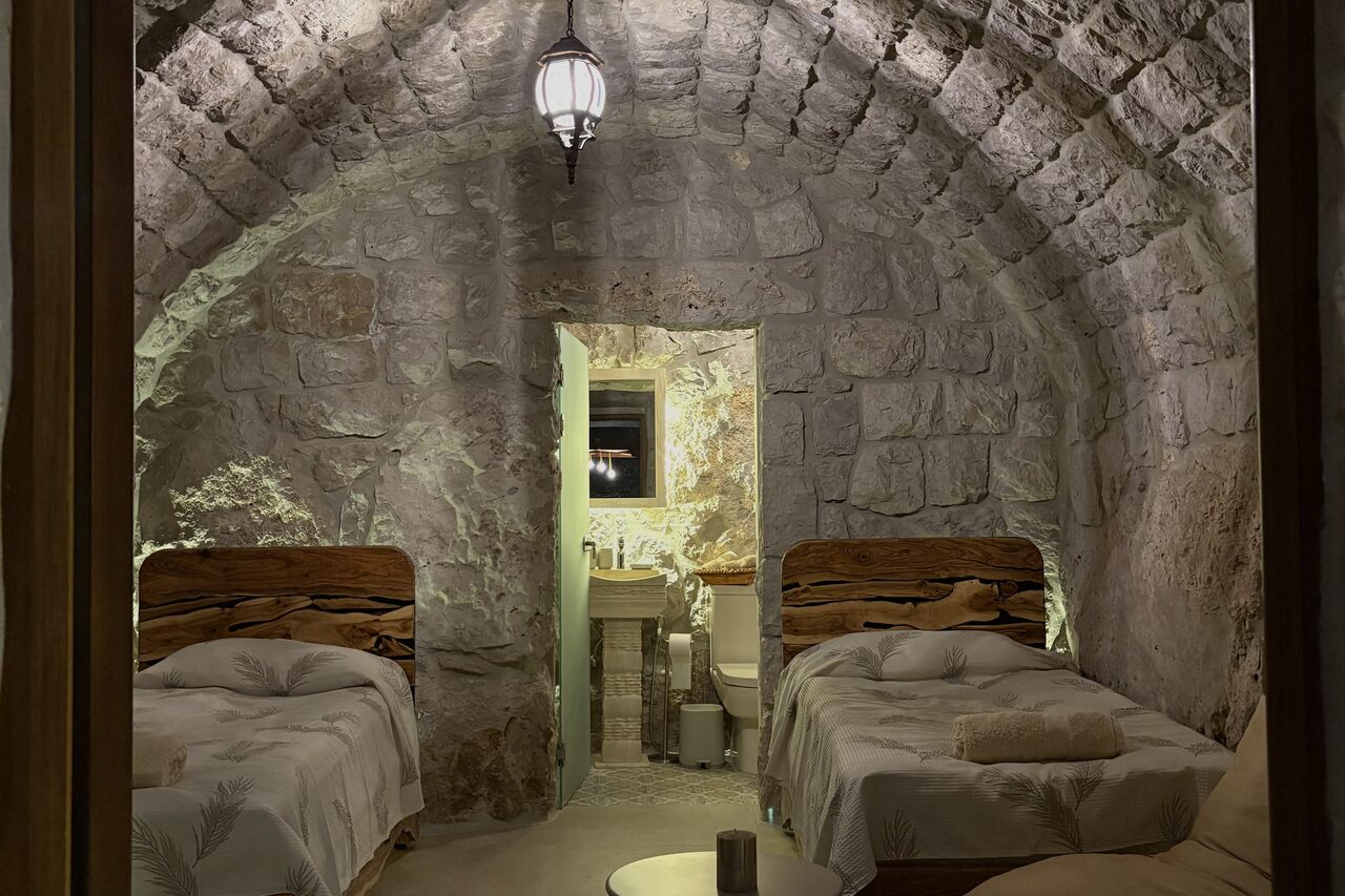 Gemelli: two matching beds facing each other under the vaulted stone ceiling, the ensuite door open beyond them.