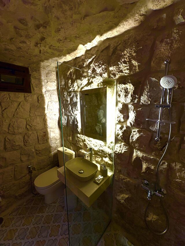 La Grande's walk-in shower, cut into the stone wall with a glass panel and a lit mirror.