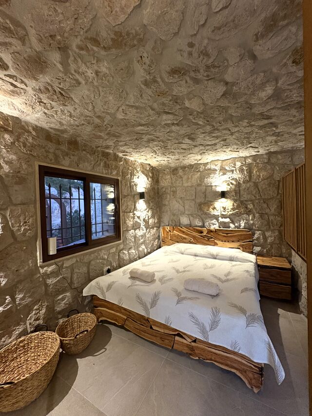 The bed in La Grande, raw timber frame against the stone wall beneath the window.