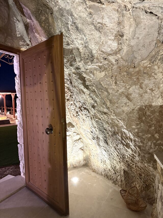 The timber door into La Grotta, set into the rock face with the terrace lights visible outside at night.