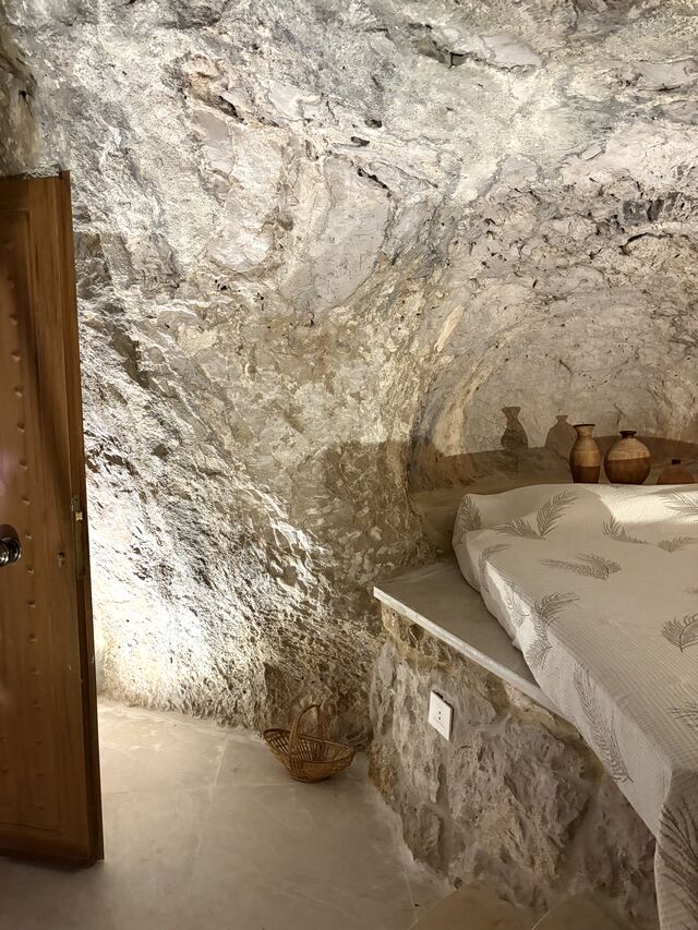 A wider view of the La Grotta bed niche, with woven baskets and clay pottery on the rock ledge beside it.
